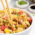 A bowl full of fried rice has chopsticks taking a piece out.