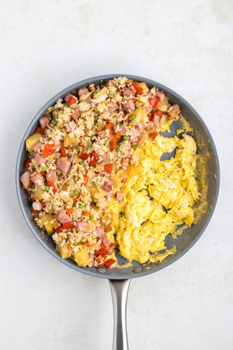 Half a pan is full of cooking egg along with rice mixture.