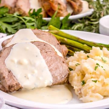 Beef Tenderloin Ina Garten, sliced on a plate with gorgonzola sauce, mashed potatoes and asparagus.