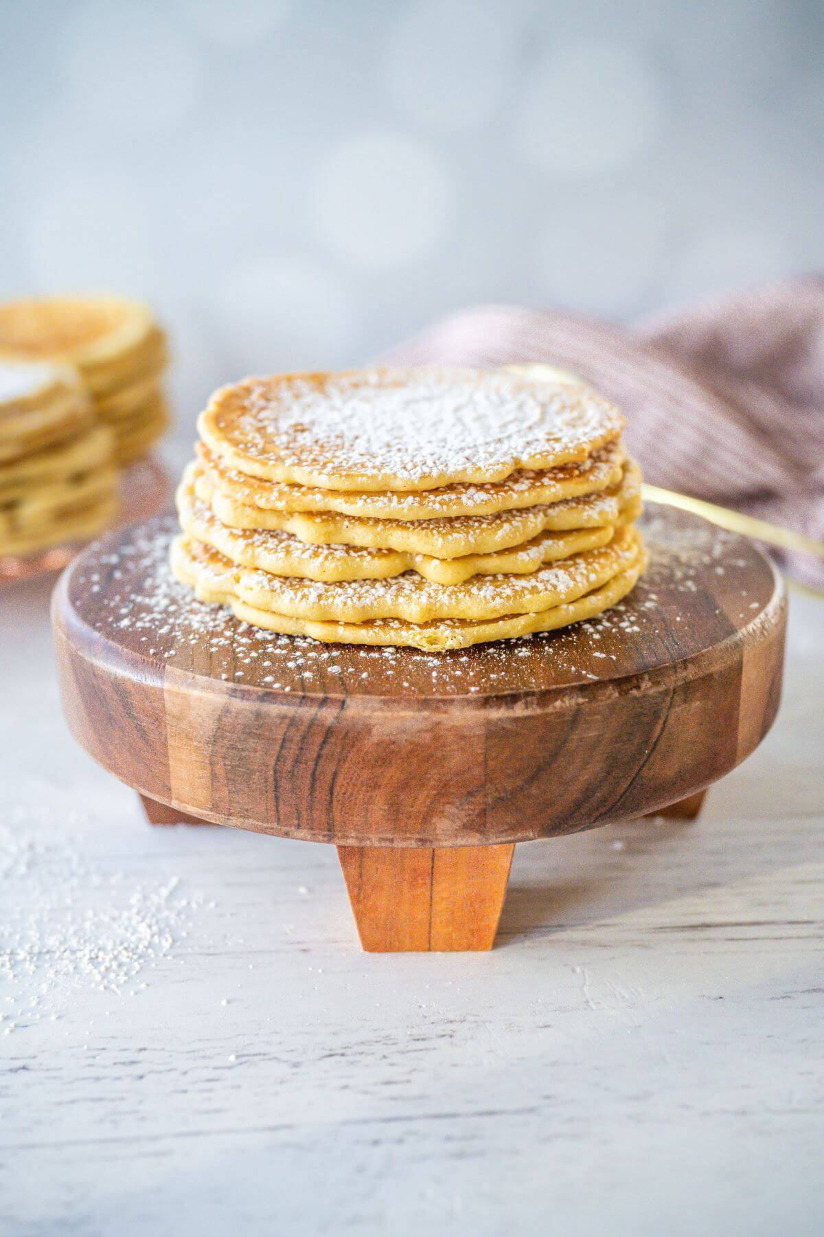 Side view of stacked cookies on wooden display plate show powder sugar garnish.