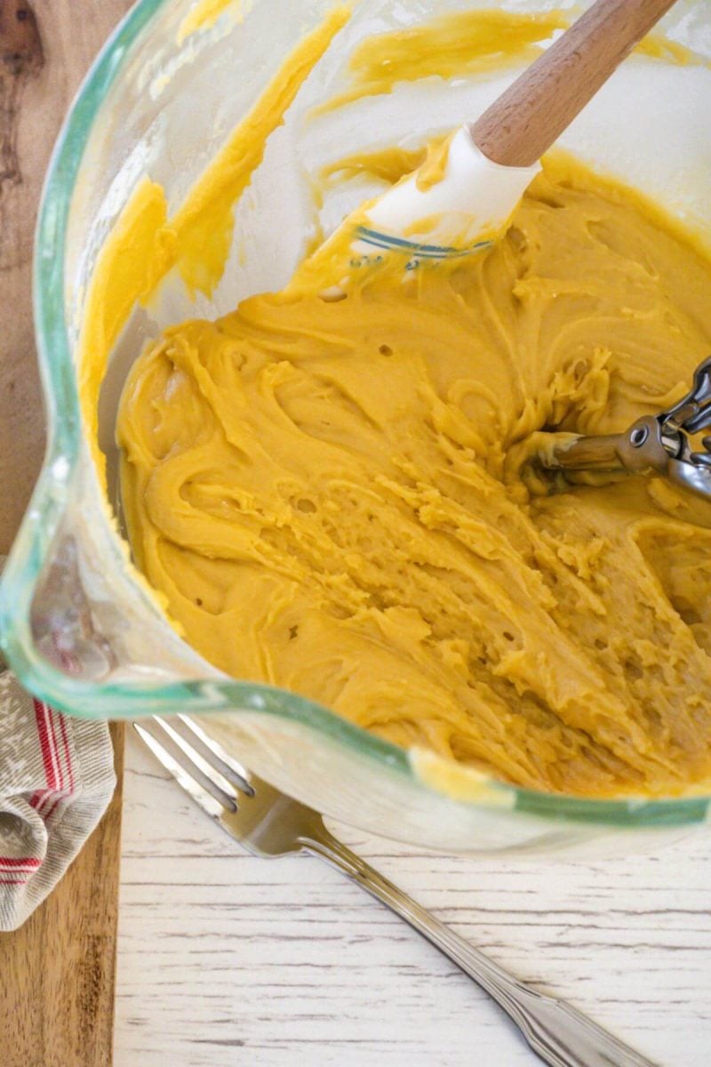 A spatula and cookie scoop rest in the mixing bowl of cookie dough.