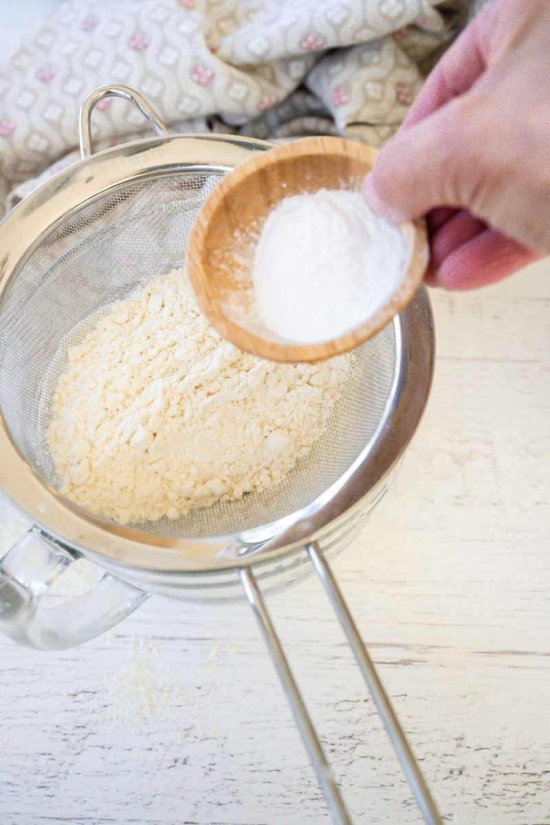 A bit of baking powder and salt are added with flour by a hand into sifter.