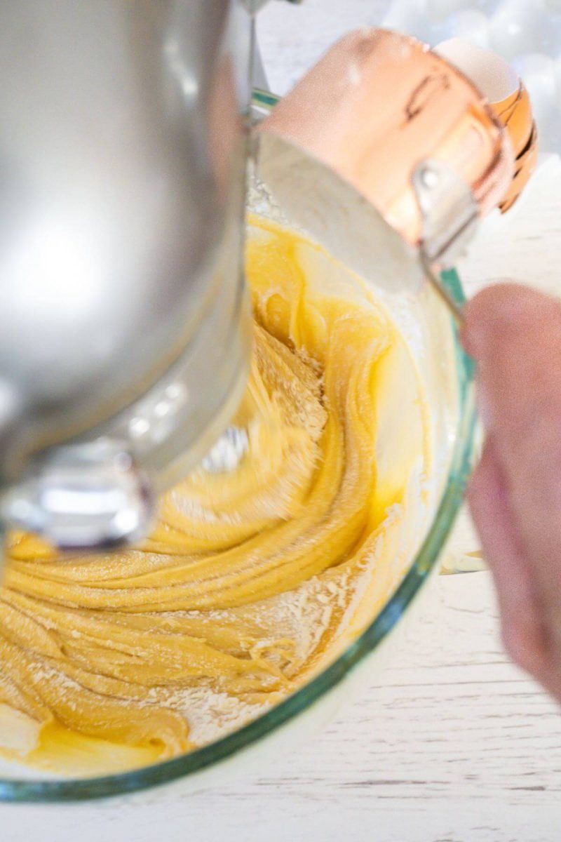 A hand pours dry ingredients into the mixing bowl mixture.