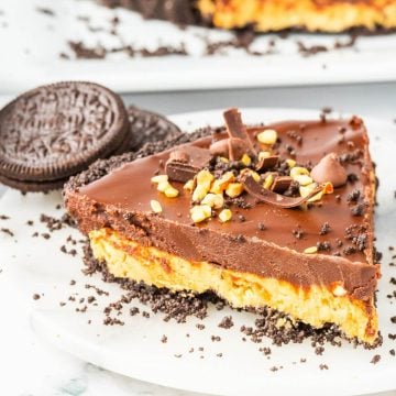 A thick slice of peanut butter Oreo pie decorated with peanuts, chocolate shavings, and Oreos on a plate.