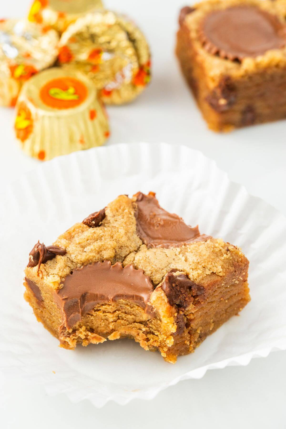 A blondie with a bite removed is in front of another blondie and Reese's peanut butter cups.