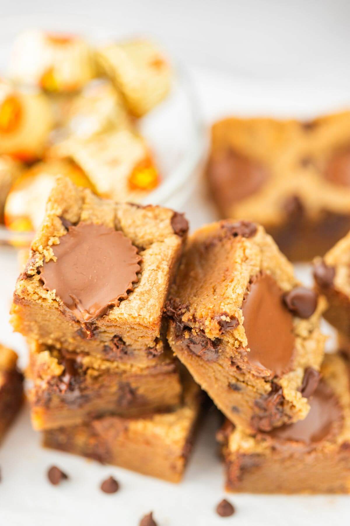 A stack of blondies sit in front of peanut butter cups in background.