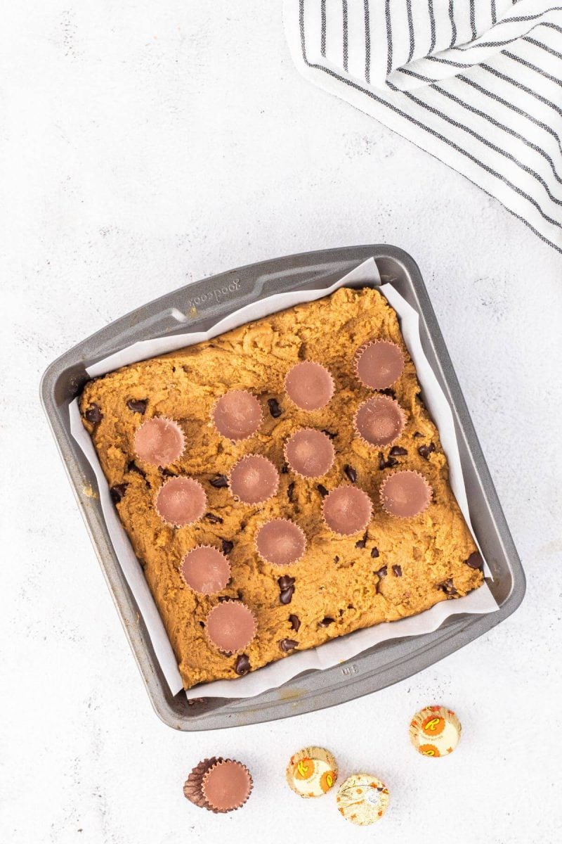 Peanut butter cups sit on surface of batter in a pan.