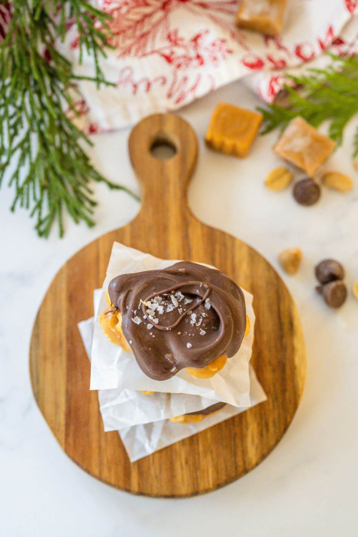 A wooden cut board is shown from top with the chocolate peanut clusters centered in the middle and surrounded by holiday decor.