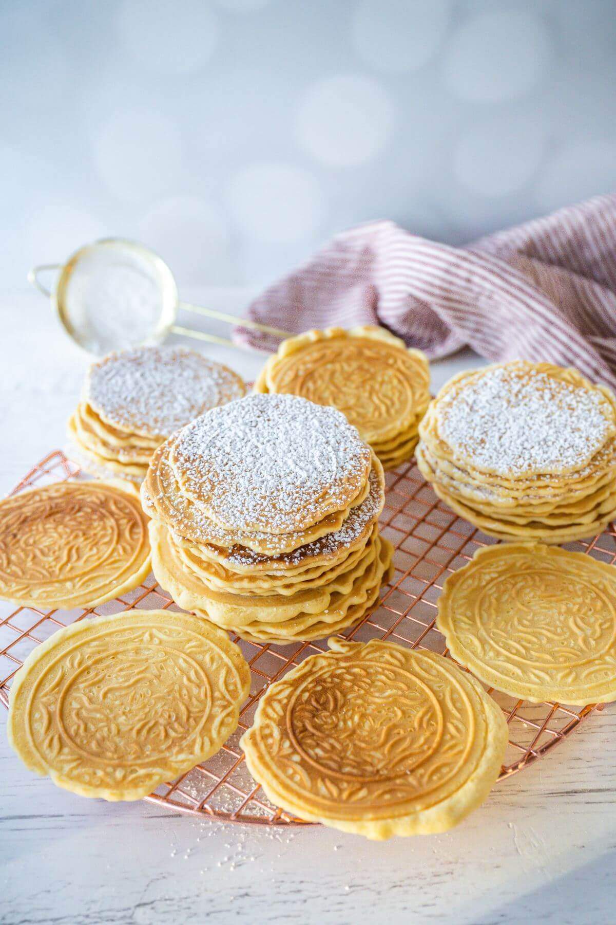 Pizzelle cookies are laying on a wire rack in various stack heights.