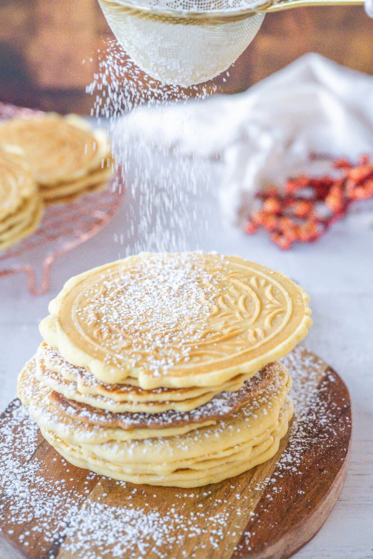 A sift shakes powdered sugar onto tower of cookies.