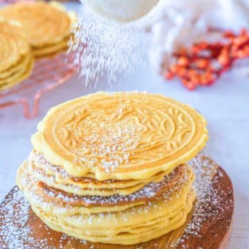 Pizzelles being dusted with powdered sugar.