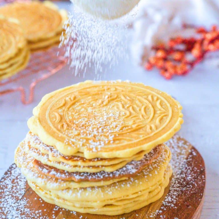 Pizzelles being dusted with powdered sugar.