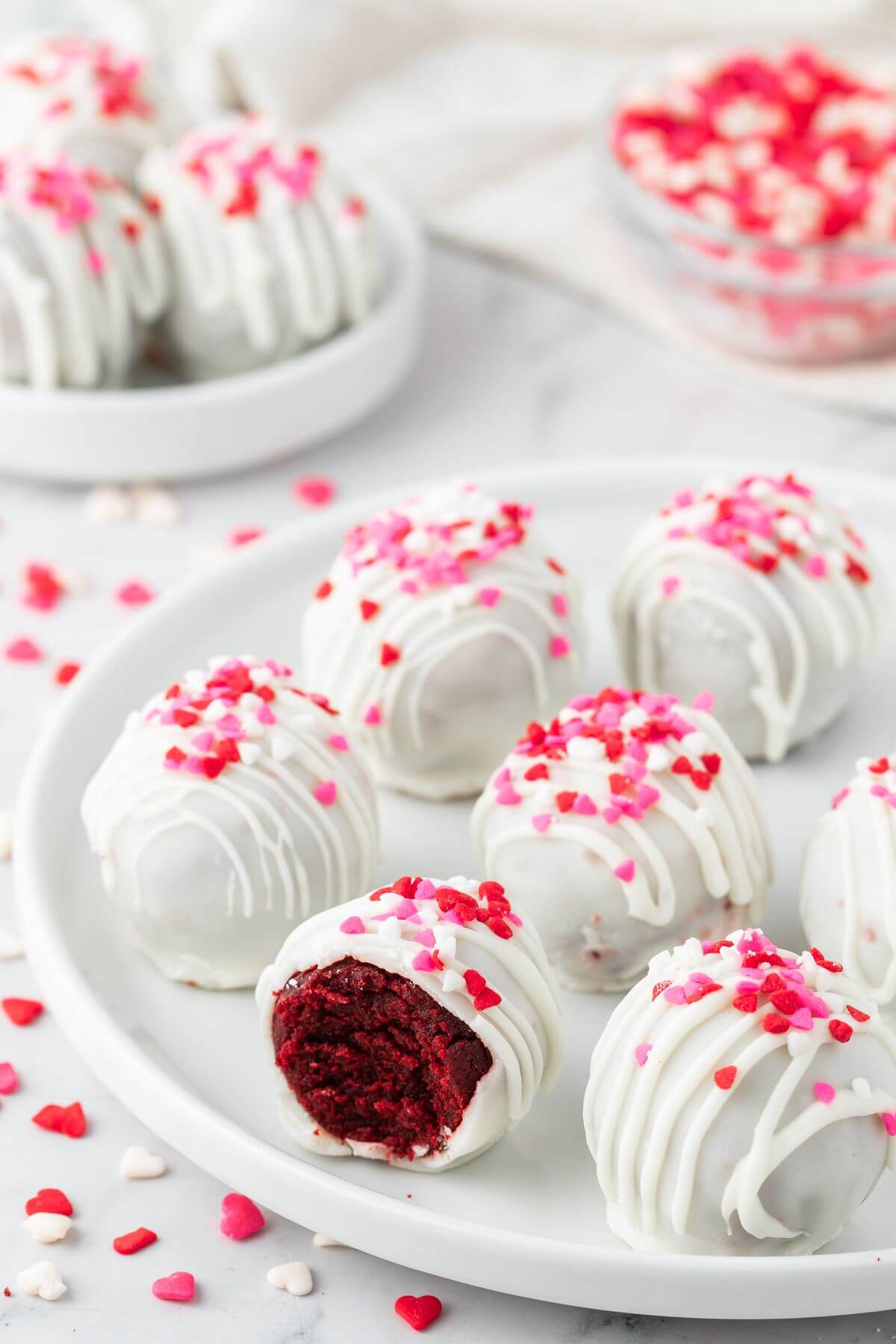 Two plates hold clusters of white, heart-sprinkled cake pops.