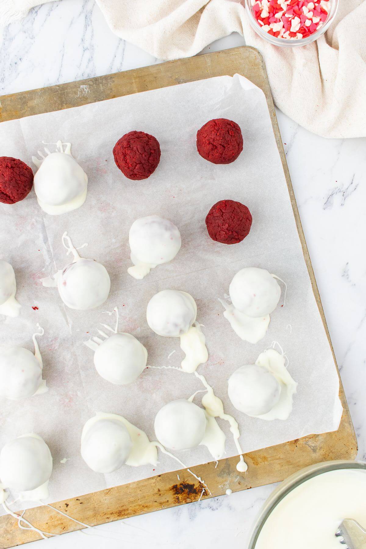 A baking sheet is covered with cake pops, mostly iced in white with a few uniced too.