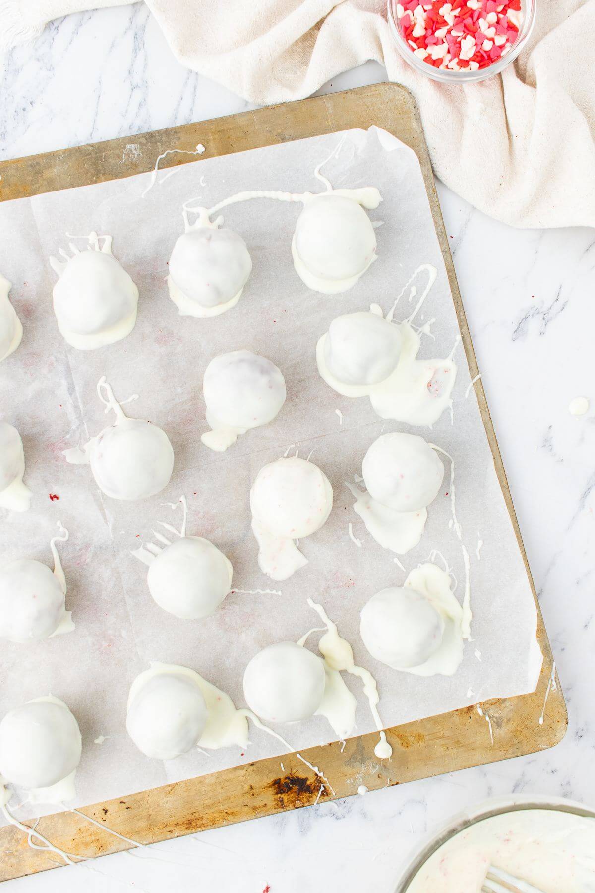 White iced cake pops cover parchment paper on a baking sheet.