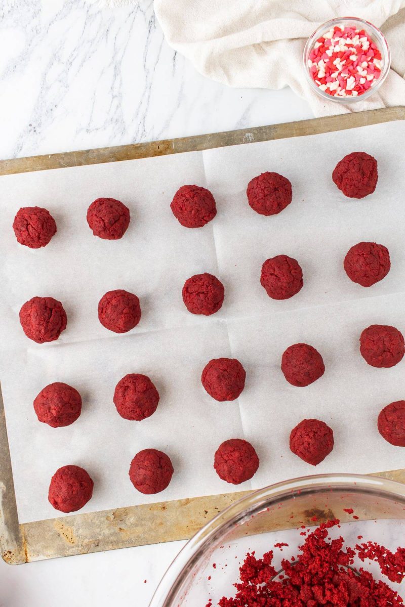 Red uniced cake pops lay in neat rows on a baking sheet.