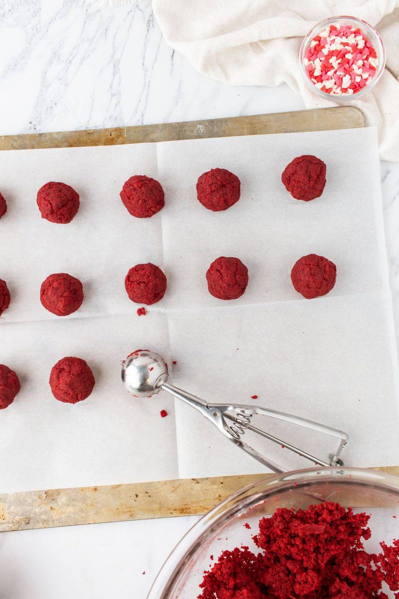 A cookie scoop drops a cake ball on a baking sheet with other cake pops.