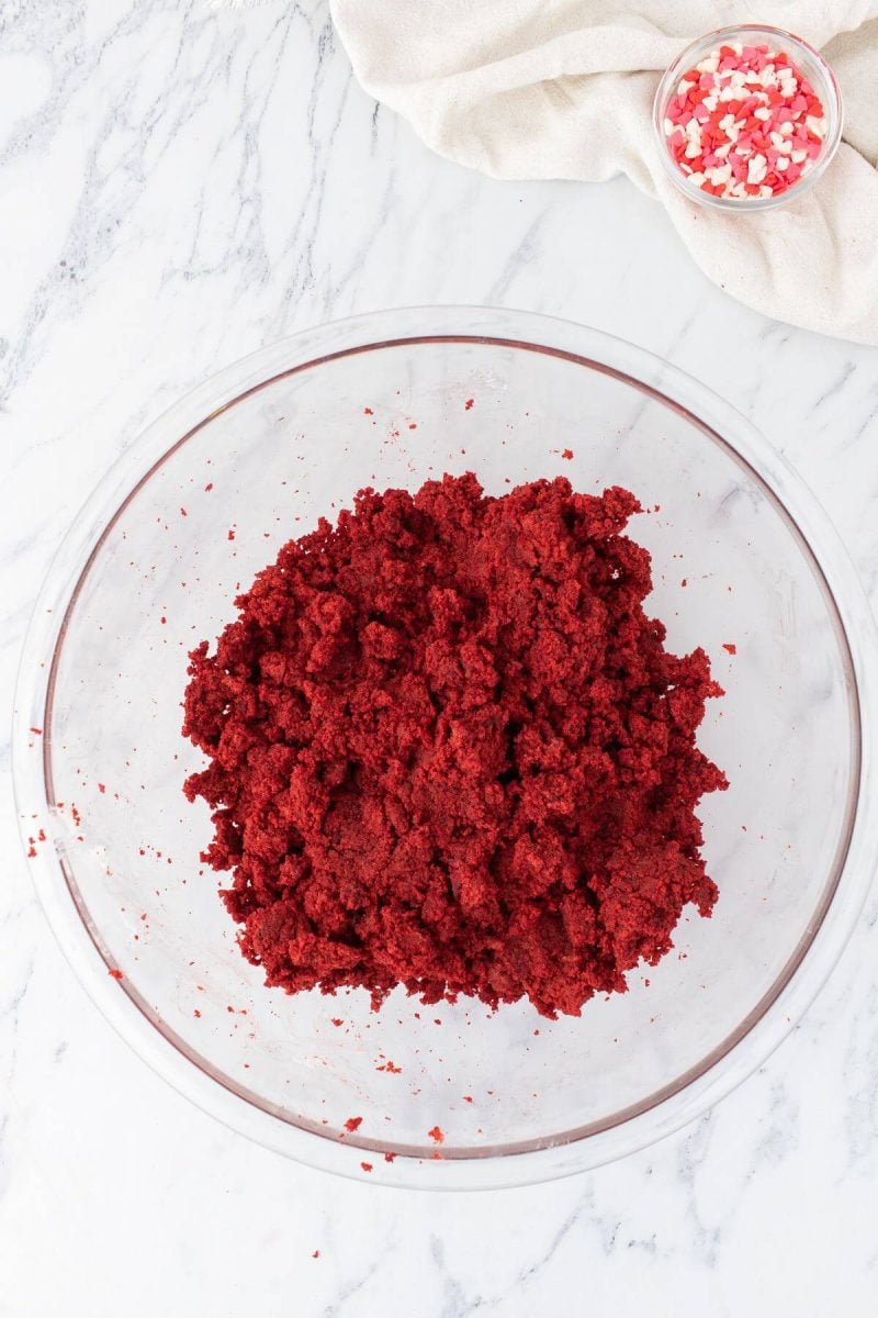 A glass bowl holds fluffy red cake mixture.