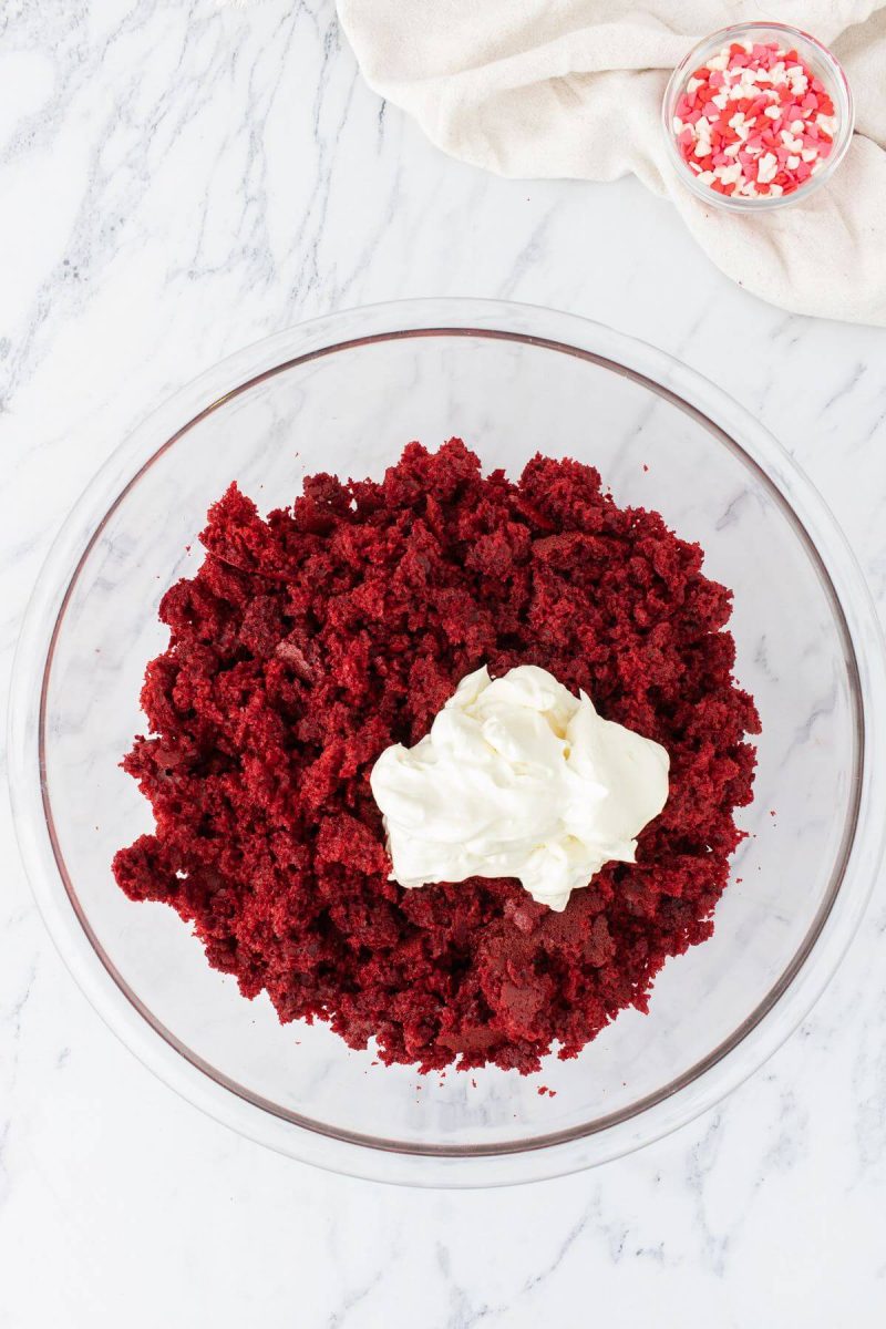 A dollop of cream cheese rests on the fluffy red cake mixture in bowl.