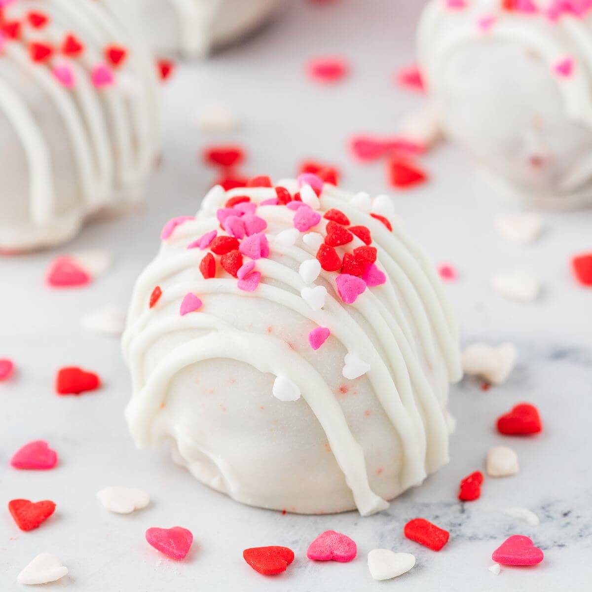 Red, pink, and white hearts sprinkles are scattered around decorated cake pops.