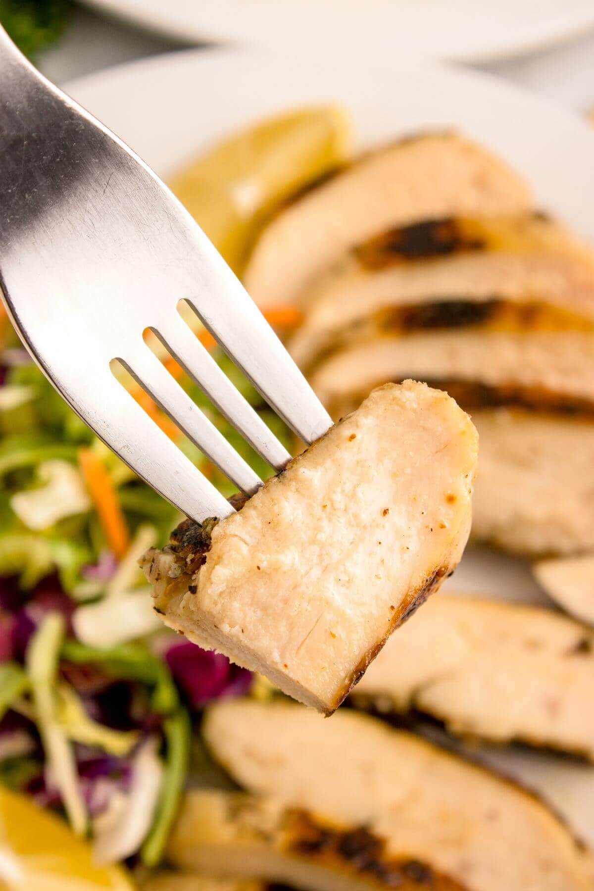 A fork holds up half a slice of chicken over the plate of food.