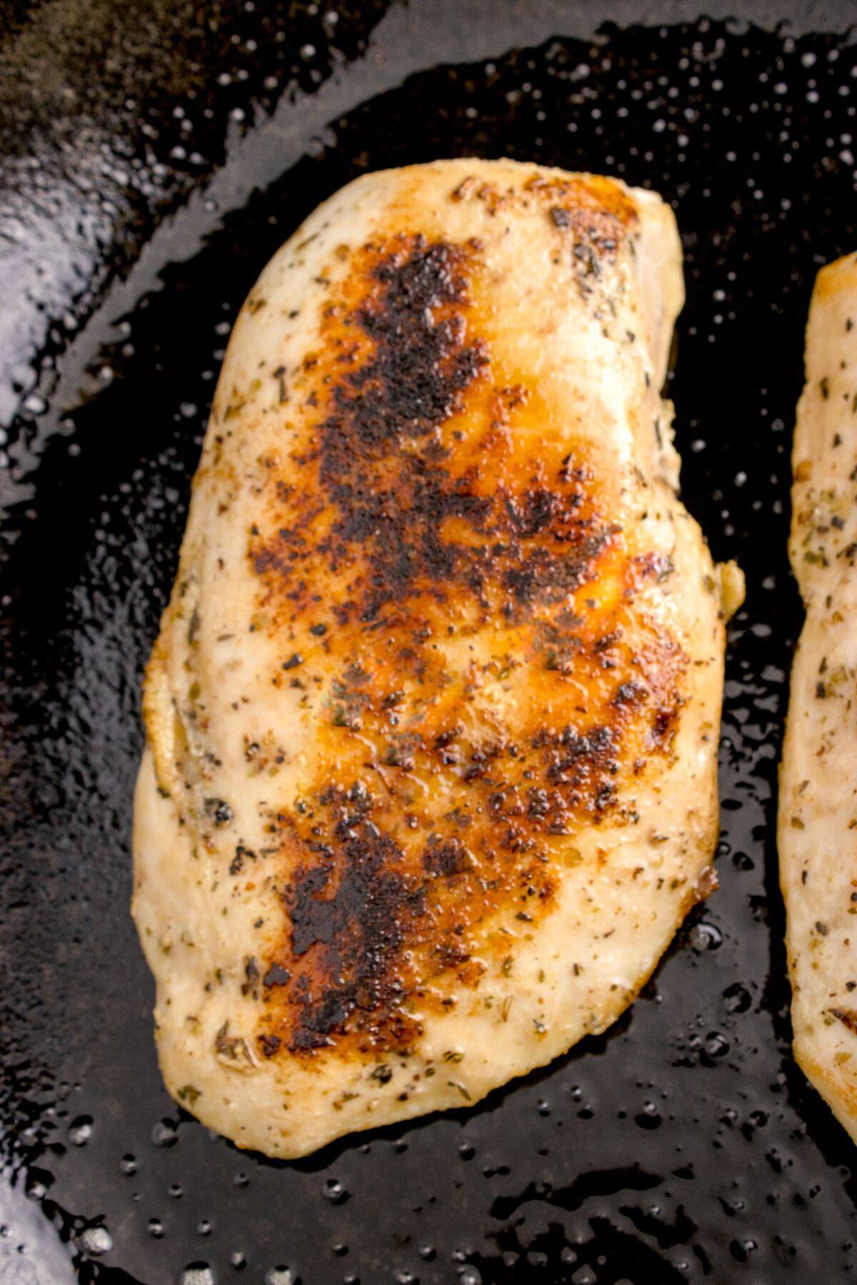A blackened sear shows on a chicken breast in pan.