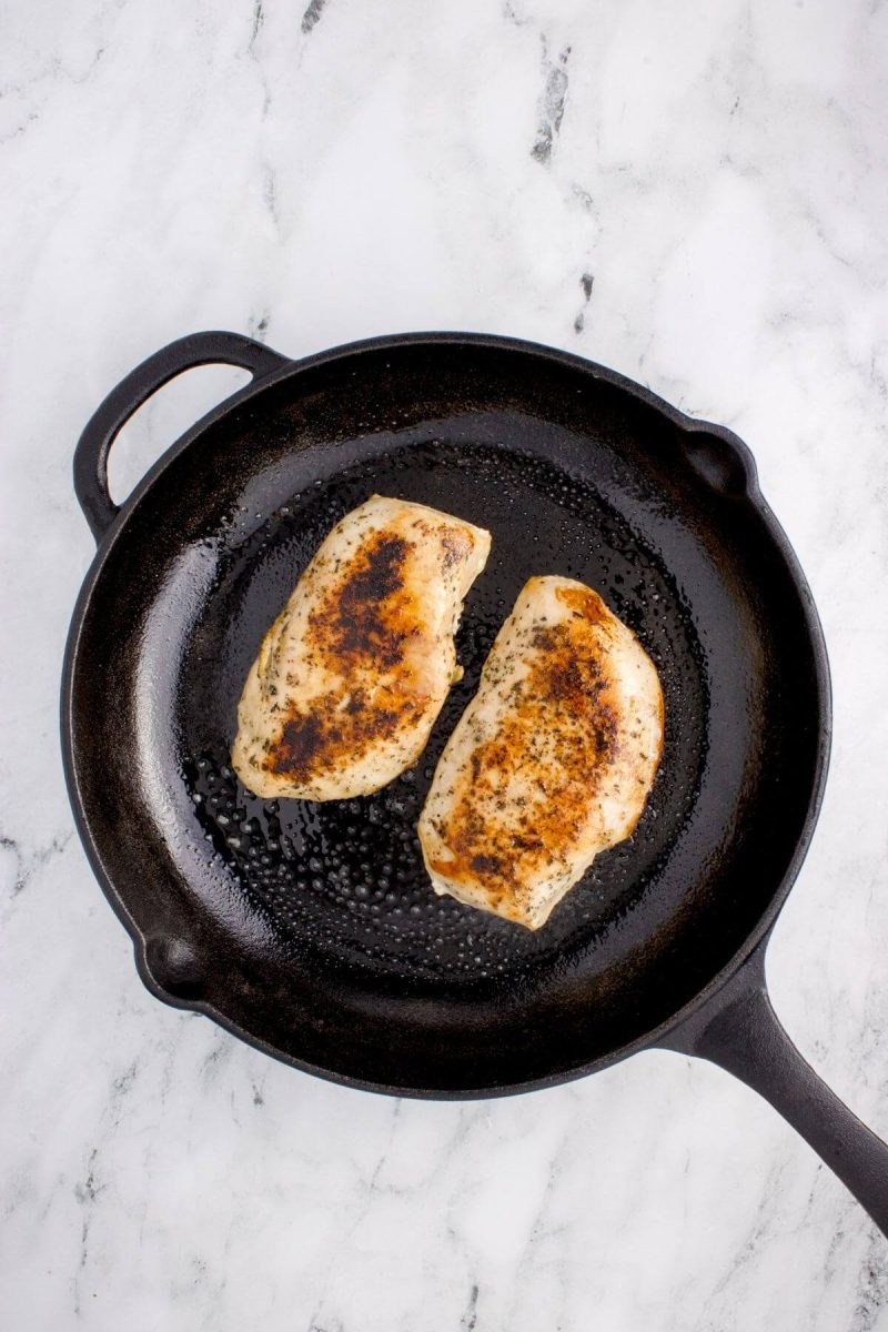 A cast iron skillet is shown from overhead with two cooked pieces of chicken.