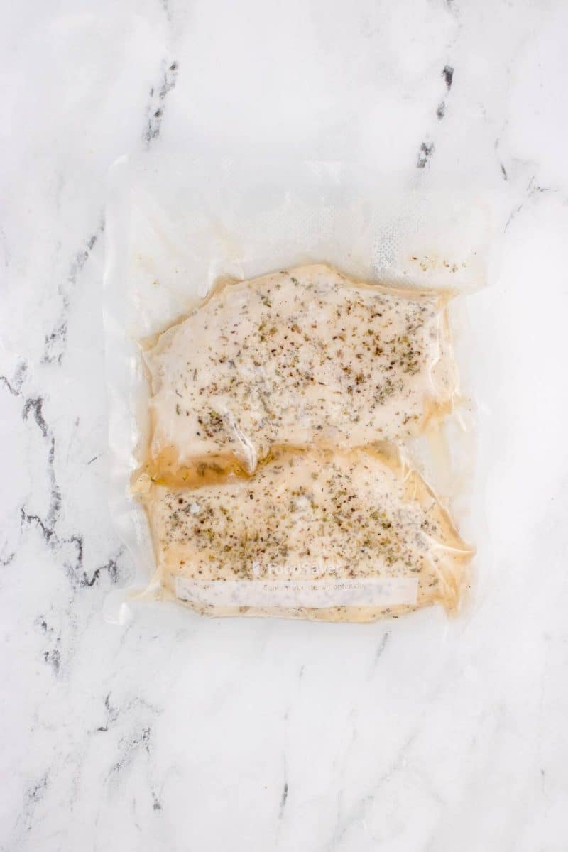 Chicken breasts and seasoning are wrapped tightly in plastic.