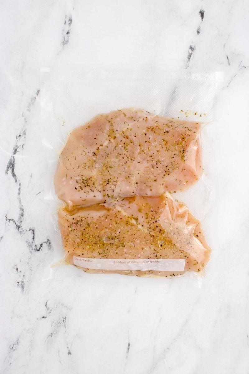 A closer view of chicken in plastic wrapping shows seasoning.