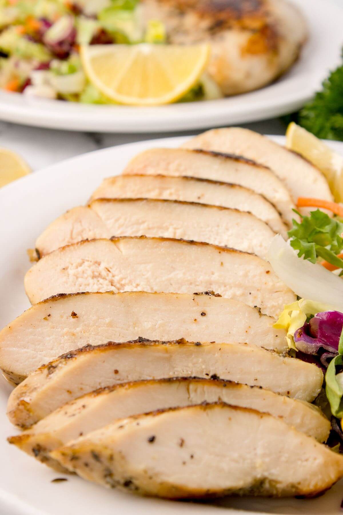 Chicken slices are spread out on plate overlapping each other next to salad.