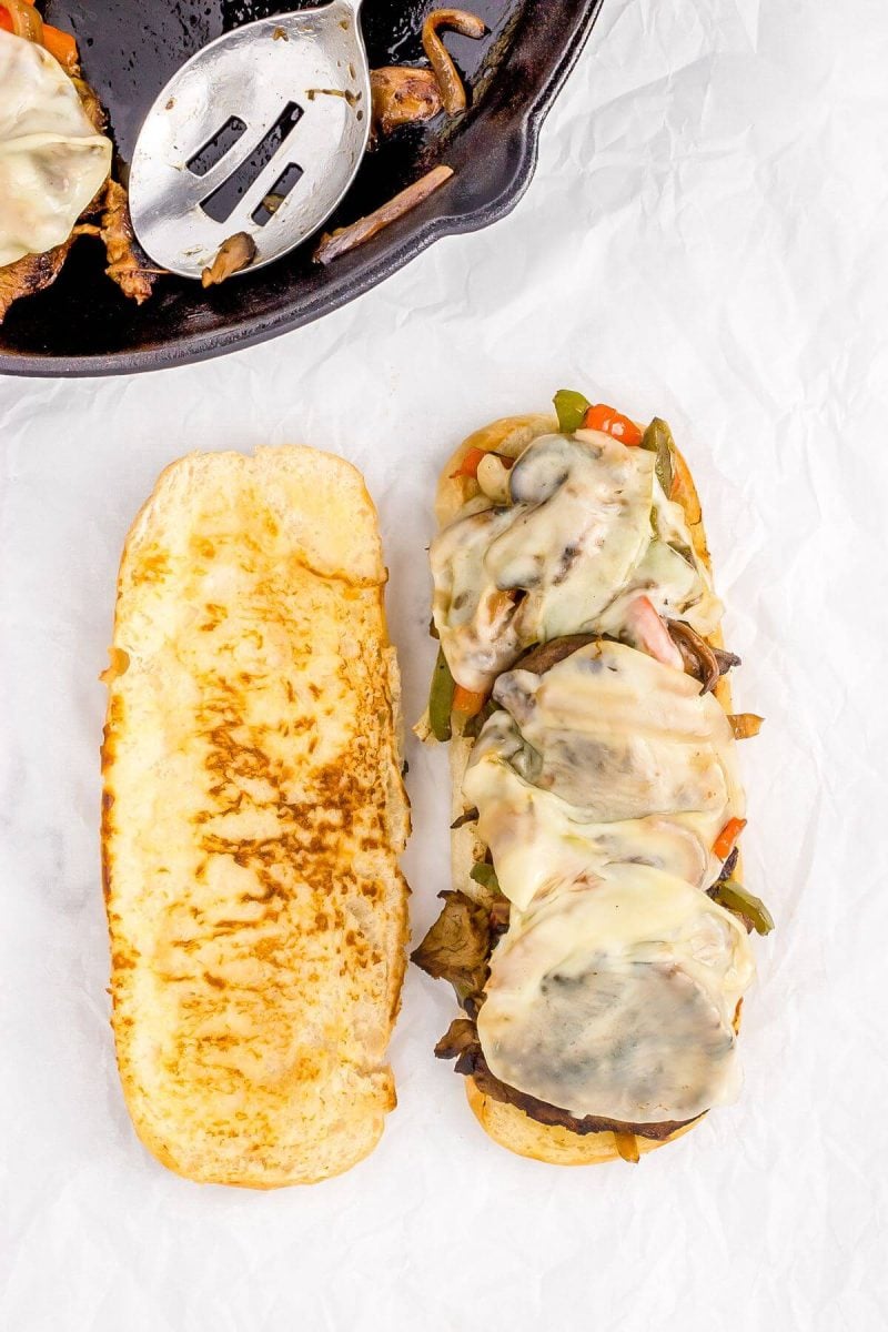 Grilled buns are shown with melted cheese on top of other fillings near skillet.