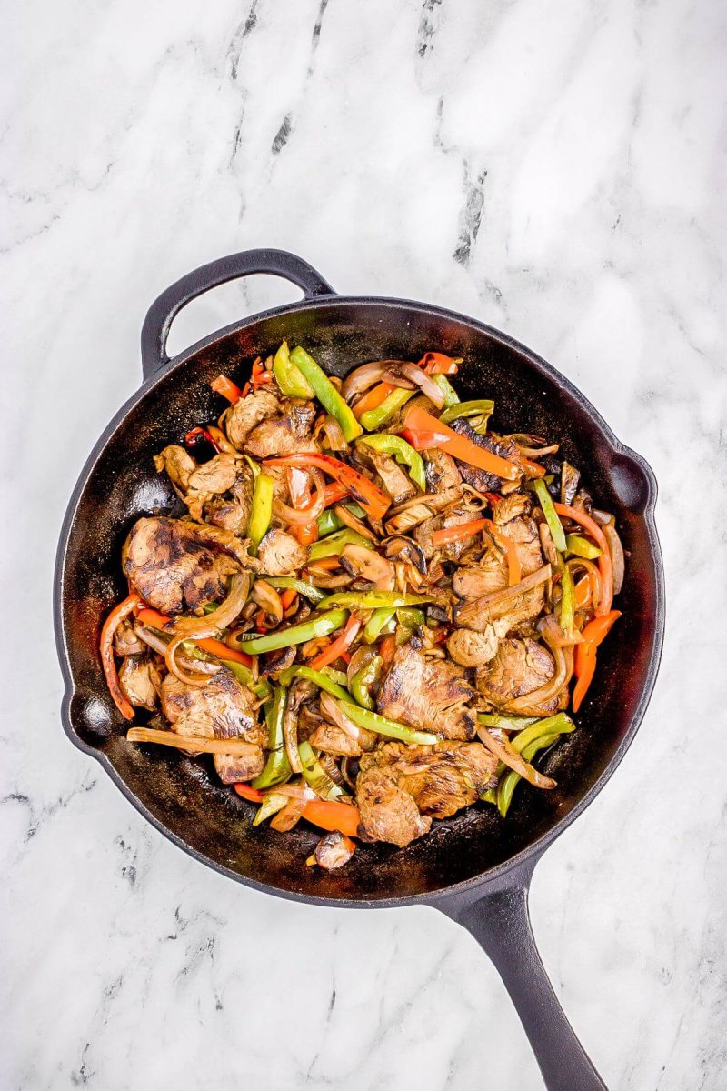 Skillet holds sliced bell peppers, mushrooms, and onions.
