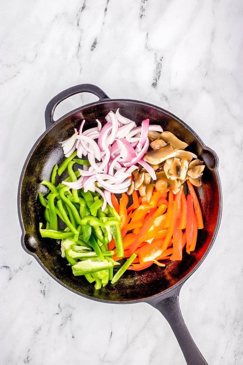 Colorful pepper, onion, and mushroom slices are in skillet.