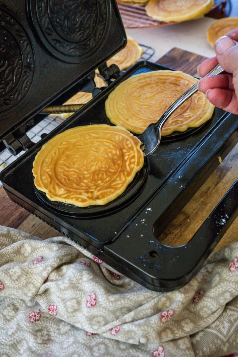 Hand using fork to remove pizzelle cookies from waffle iron. 