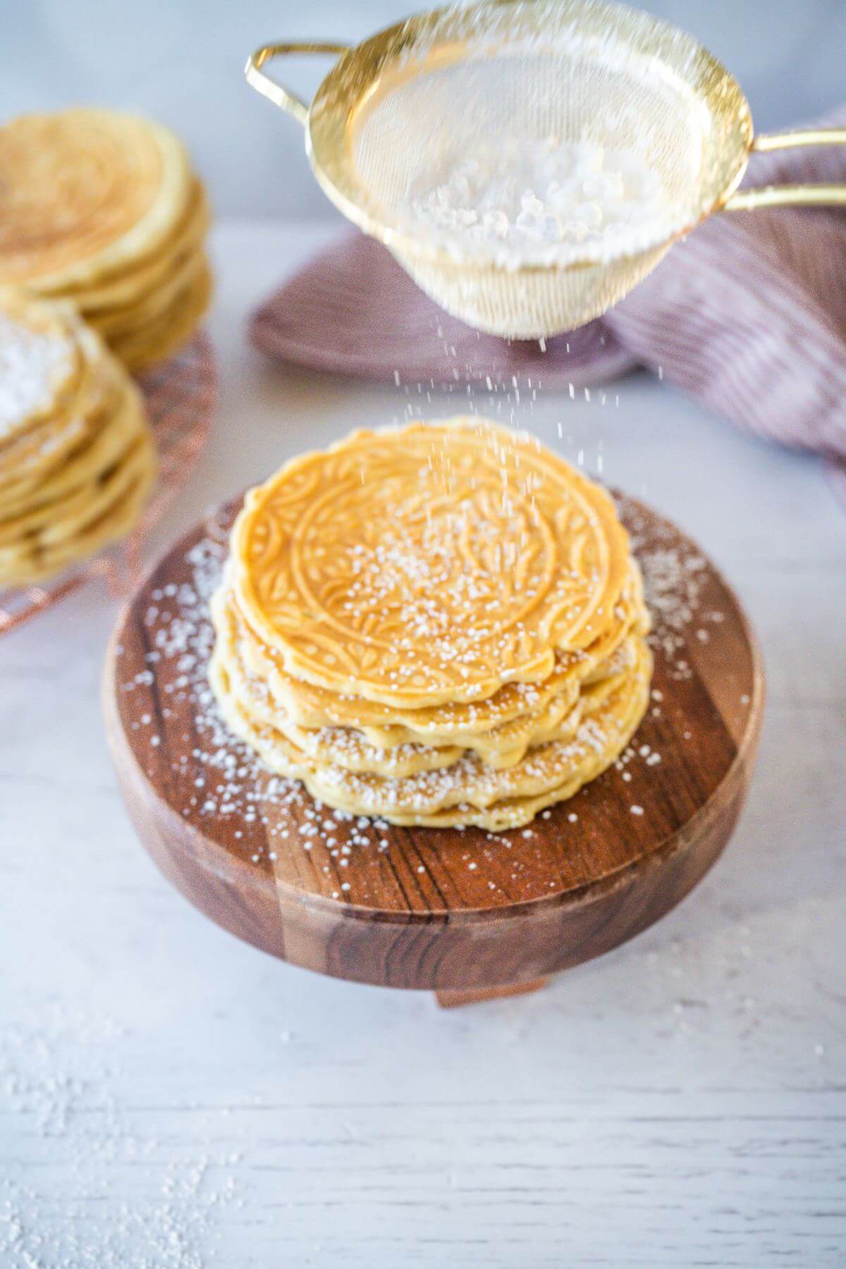 Powdered sugar is shaken from sift on top of cookie pile.