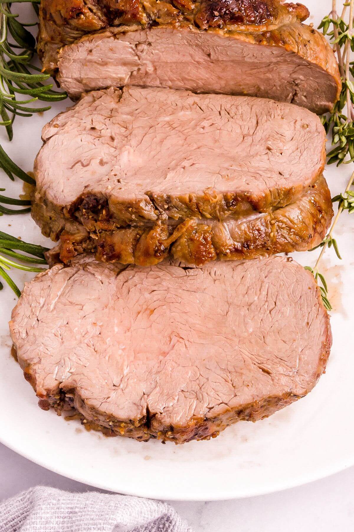 Pieces of beef are on a plate next to rosemary.