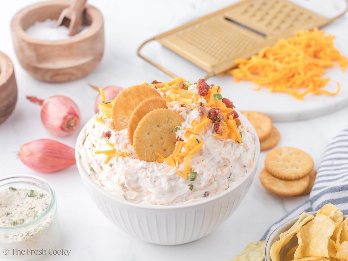 Cowboy crack dip with crackers in top, top down shot with shallots and crackers in background.