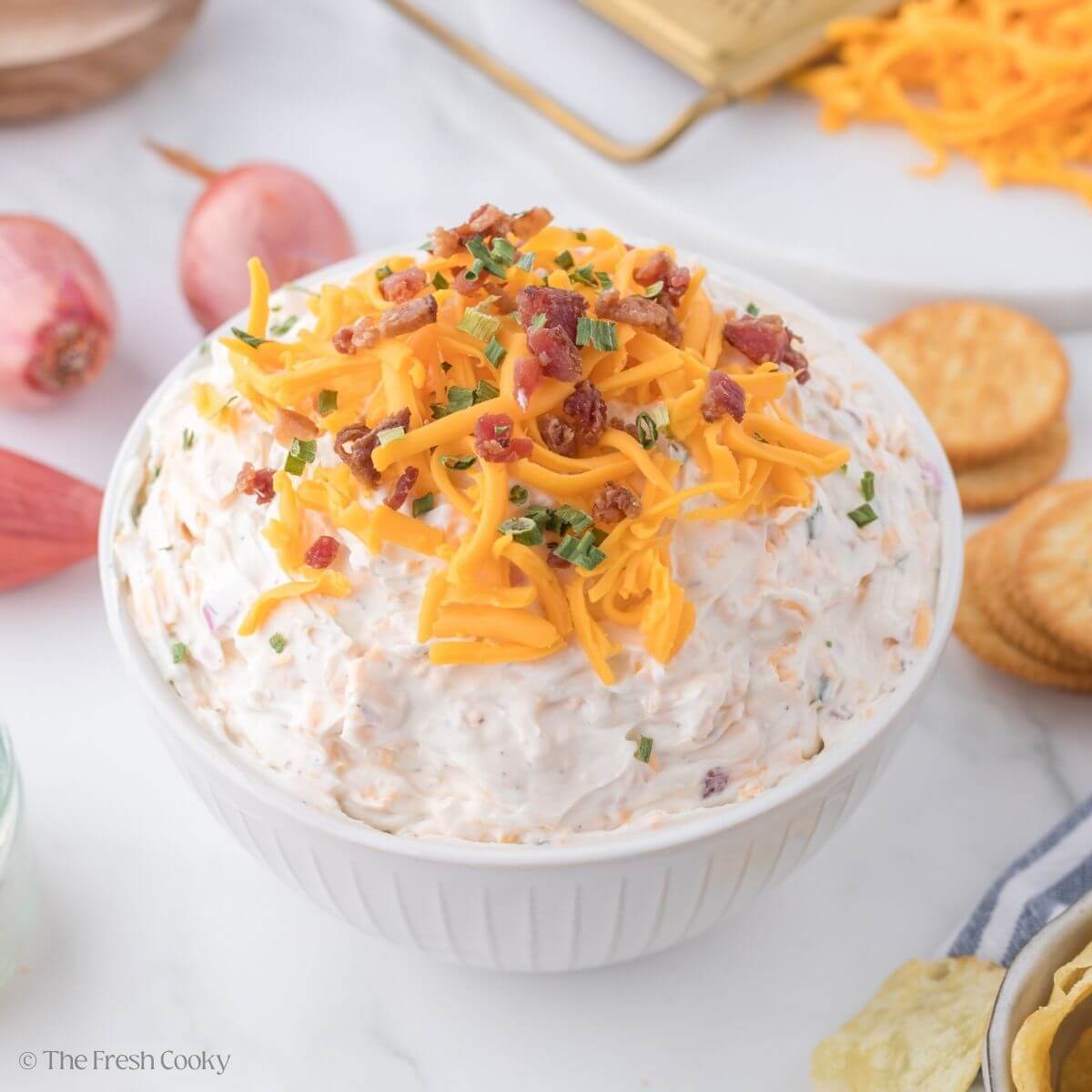 Cowboy crack dip in small bowl topped with cheddar cheese and bacon bits.