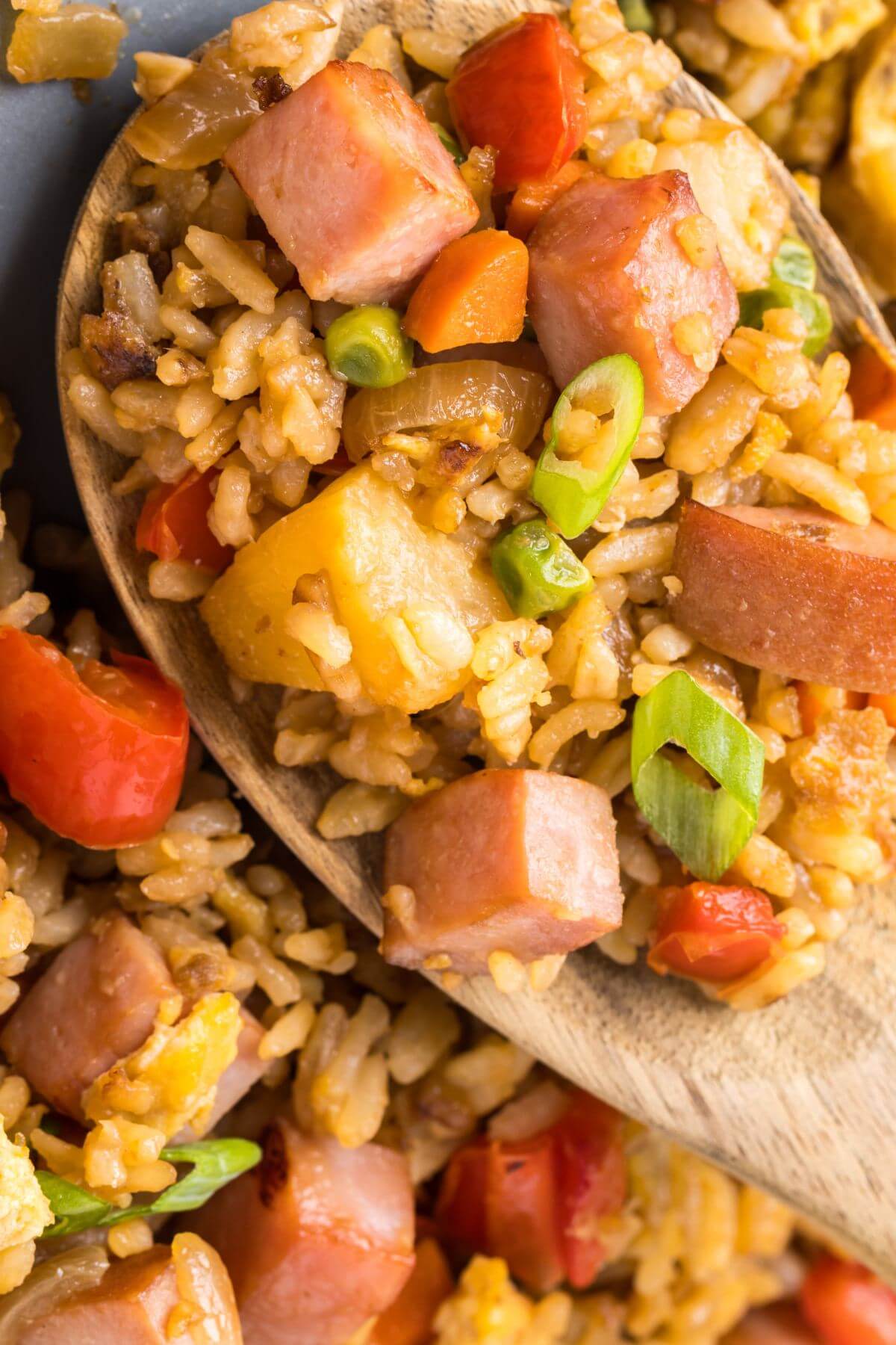 Fried rice, ham and pineapple sit on a wooden spoon.