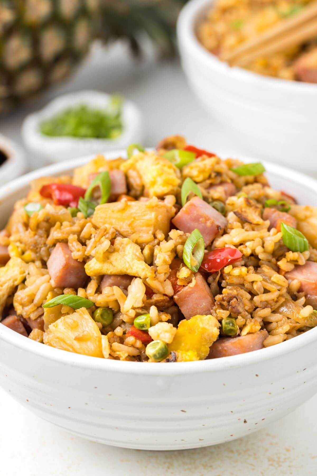 A big, full bowl of fried rice sits in front of pineapple and another bowl.