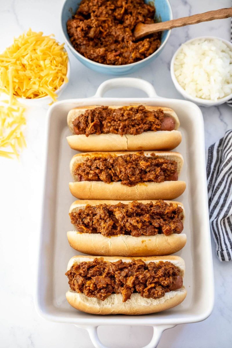 A casserole dish is filled with chili topped hot dogs.