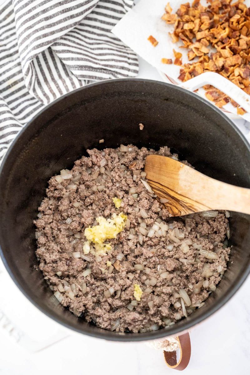 Cooked ground beef crumbles are getting mixed with minced garlic.