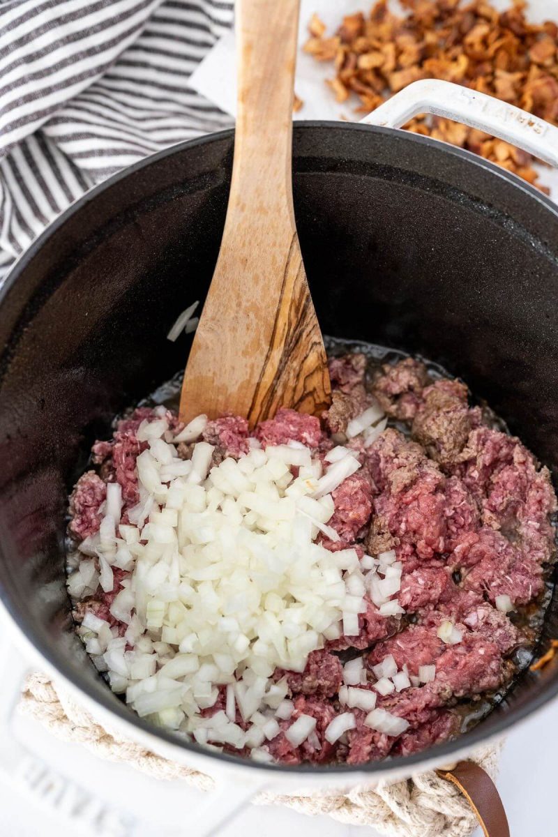 Raw onions are mixed in with ground beef in large pot.