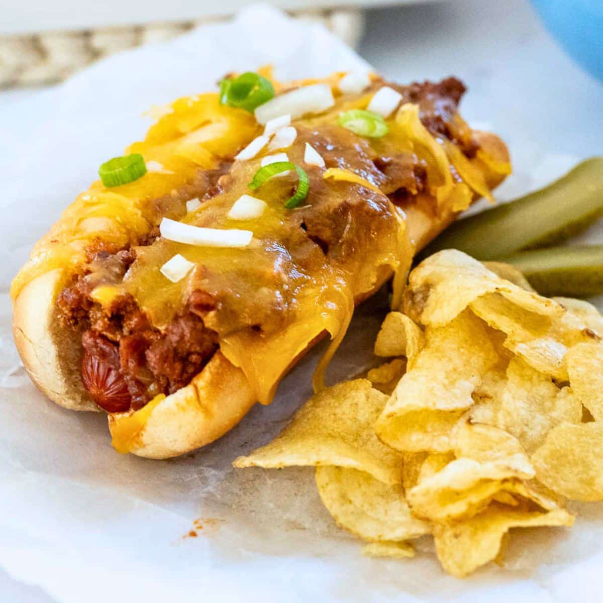Baked chili cheese dog on a plate with potato chips and pickle spears.