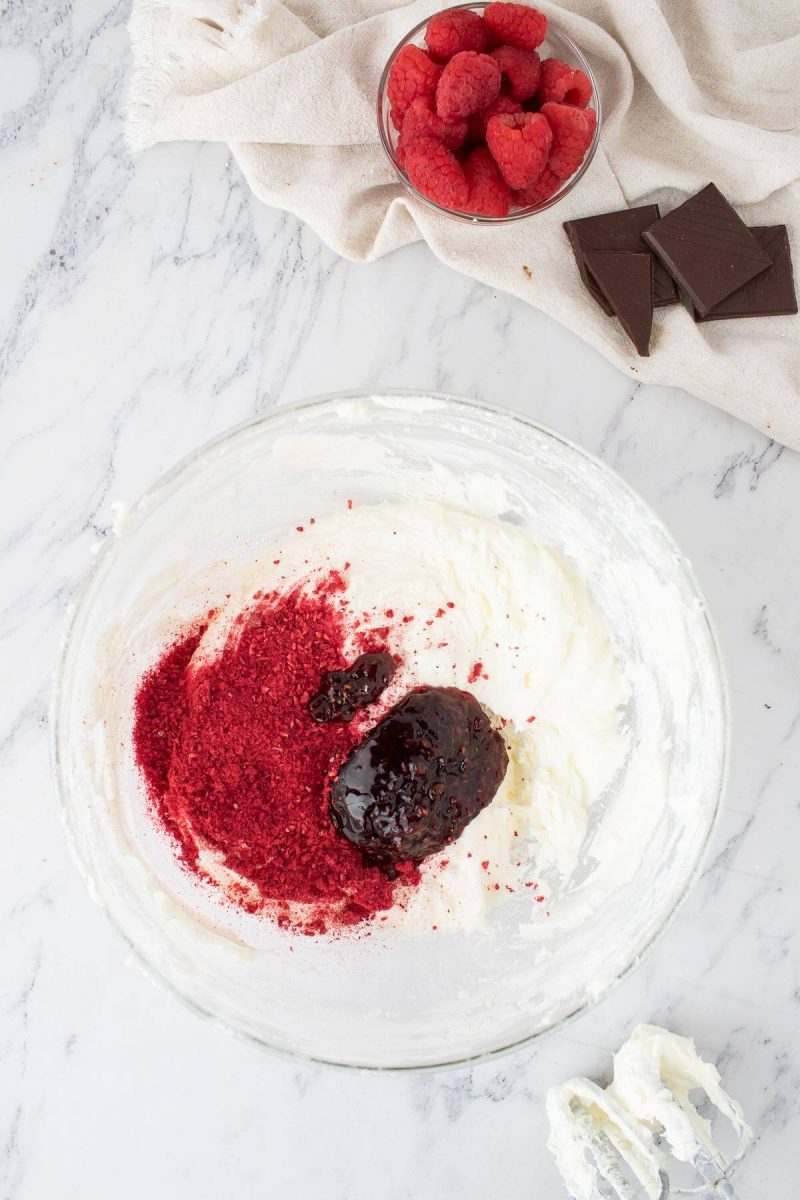 White butter icing in a glass bowl is topped with dried raspberry powder and preserves.
