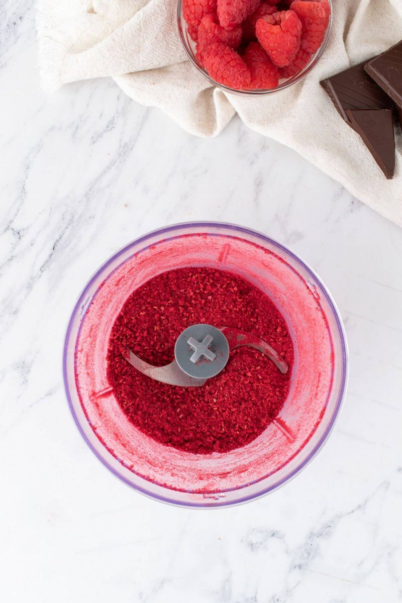 Dark pink powder from dried raspberries fills a food processor.