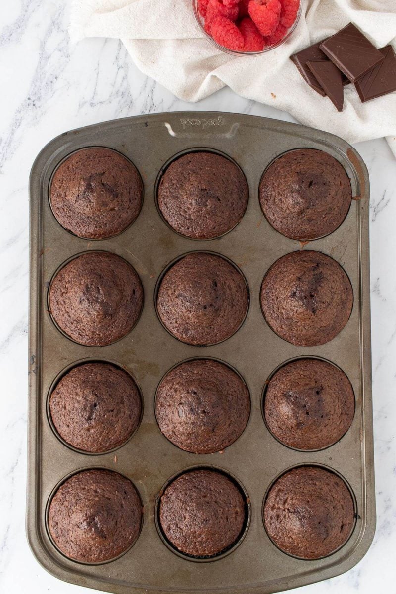 Baked dark brown chocolate cupcakes fill a cupcake pan.