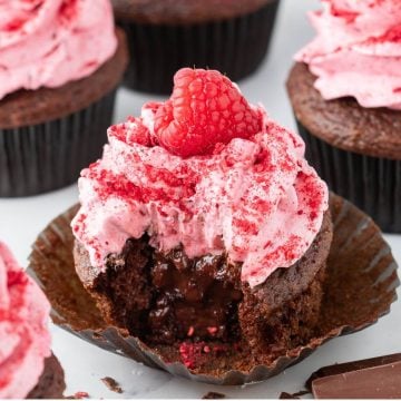 Chocolate ganache comes out of middle of pink-iced cupcake after bite taken out.