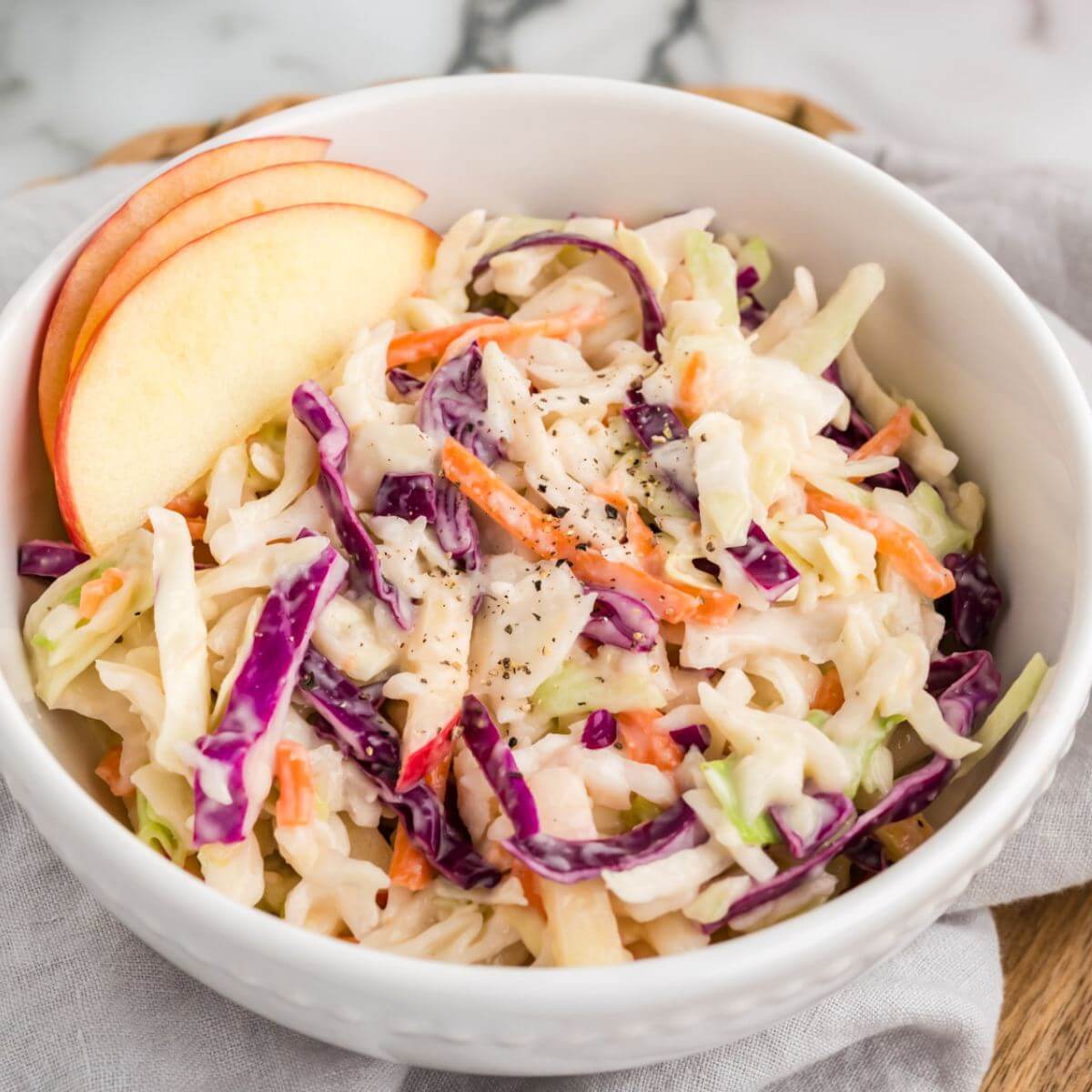 A full bowl of coleslaw includes neat apple slices on side.
