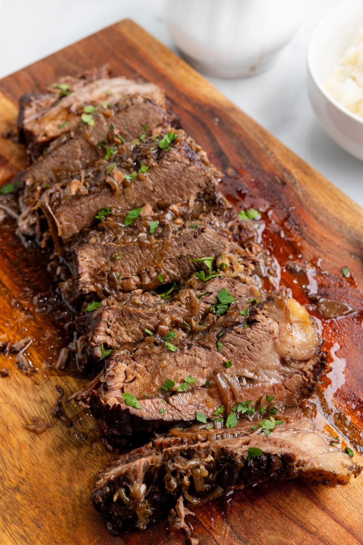 Cooked brisket is garnished with herbs on a wooden cutting board.